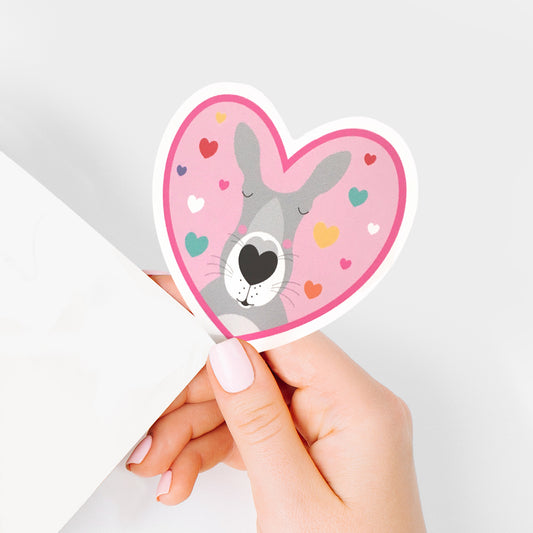 hand holding vinyl sticker of pink heart with kissing kangaroo