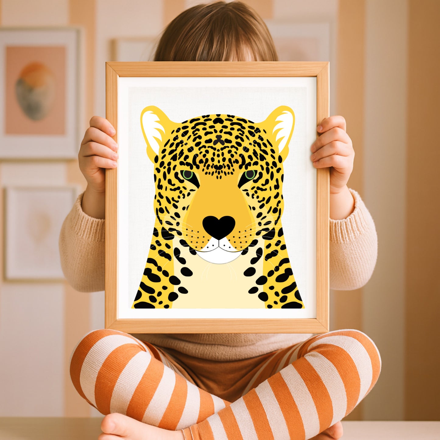 Child holding a framed illustration of a leopard in a room with framed pictures on the wall.