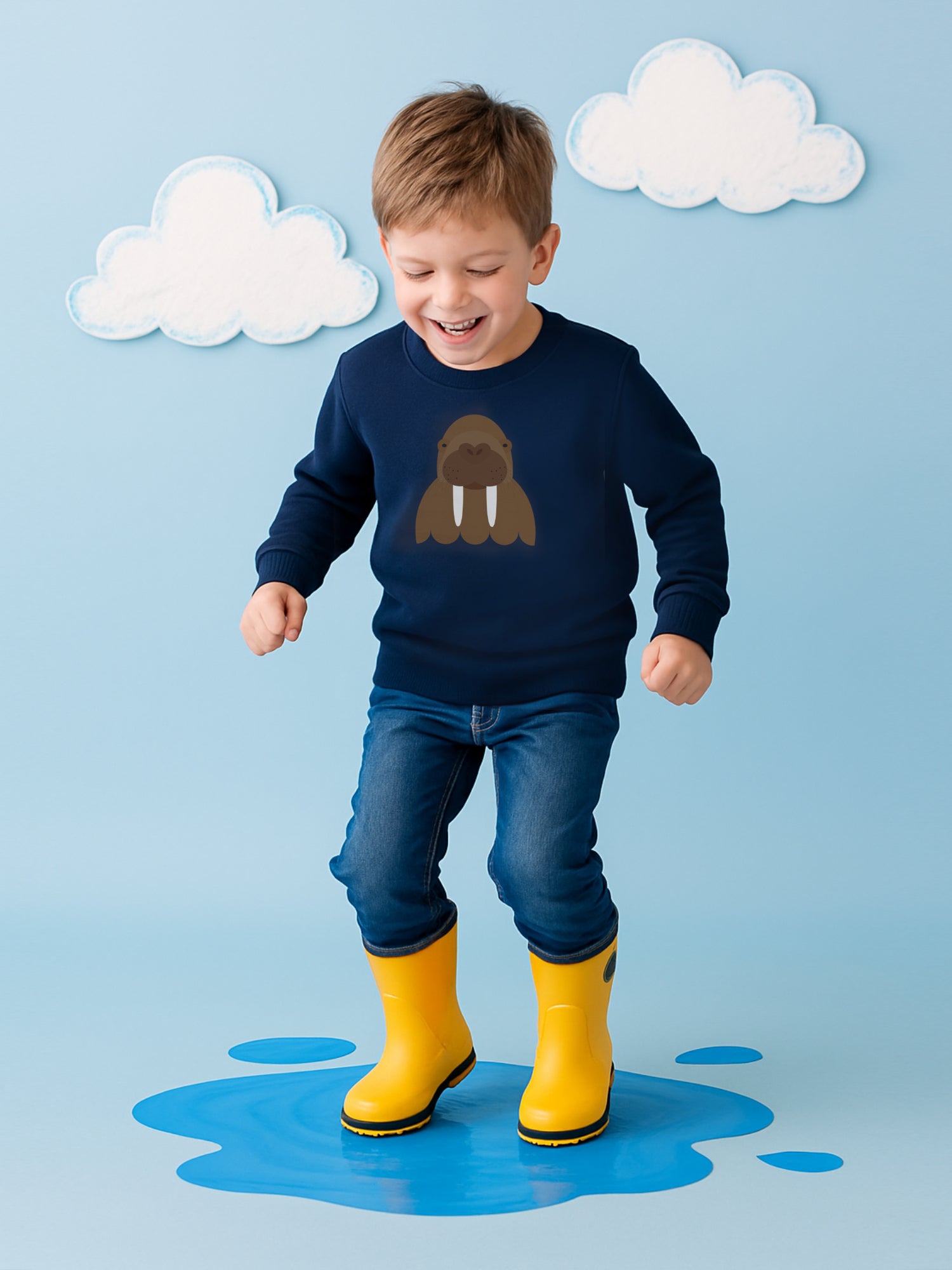 Boy splashing in puddle wearing navy jumper with walrus design