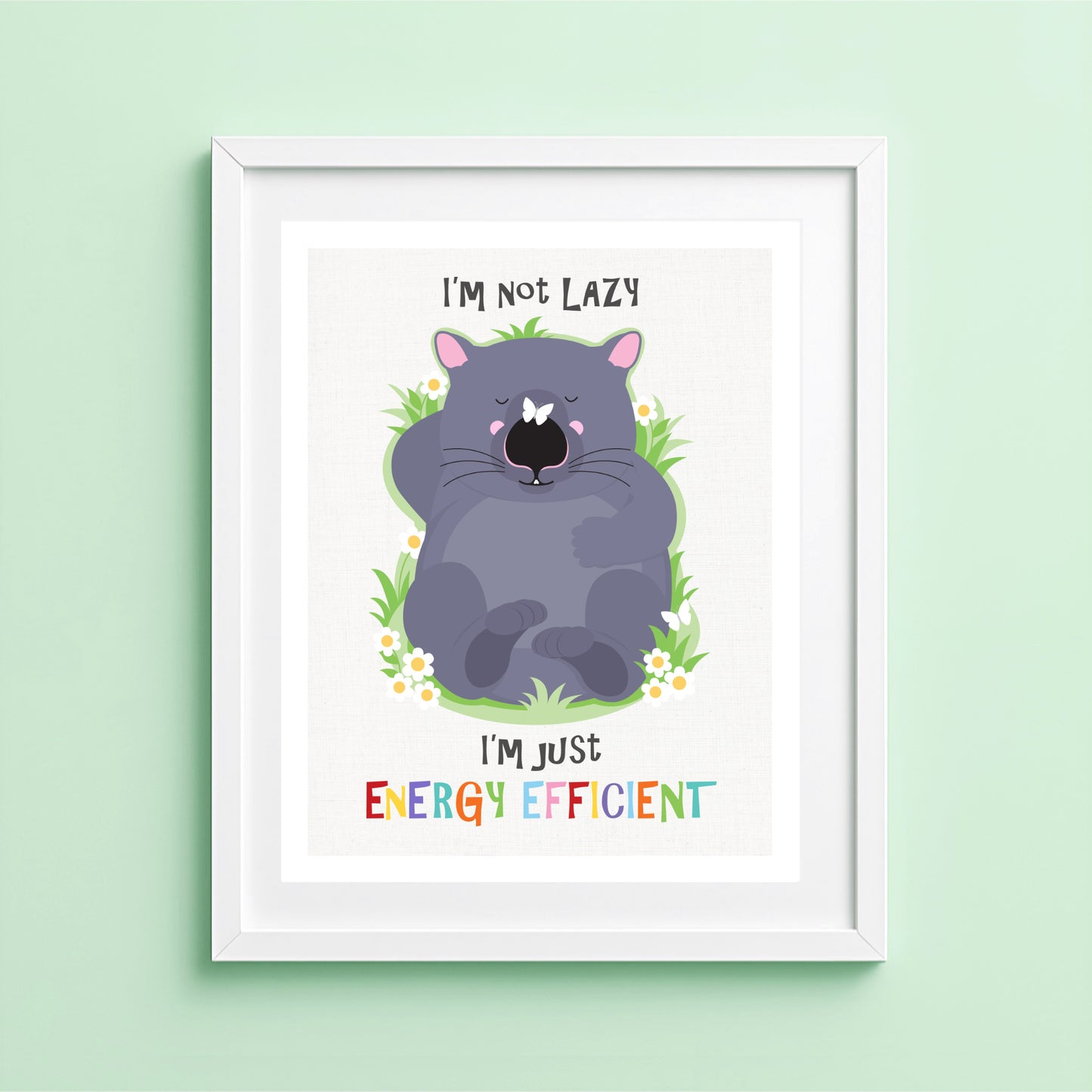 A cute illustrated wombat lies flat on his back, eyes closed, looking completely relaxed. The wombat is surrounded by a simple patch of green grass with a few small white daisies, set against a soft neutral background. Above and below the illustration, the text reads “I’m not lazy, I’m just energy efficient” in playful lettering. The overall style is flat, friendly, and minimal, with solid colours and a gentle, feel-good tone.