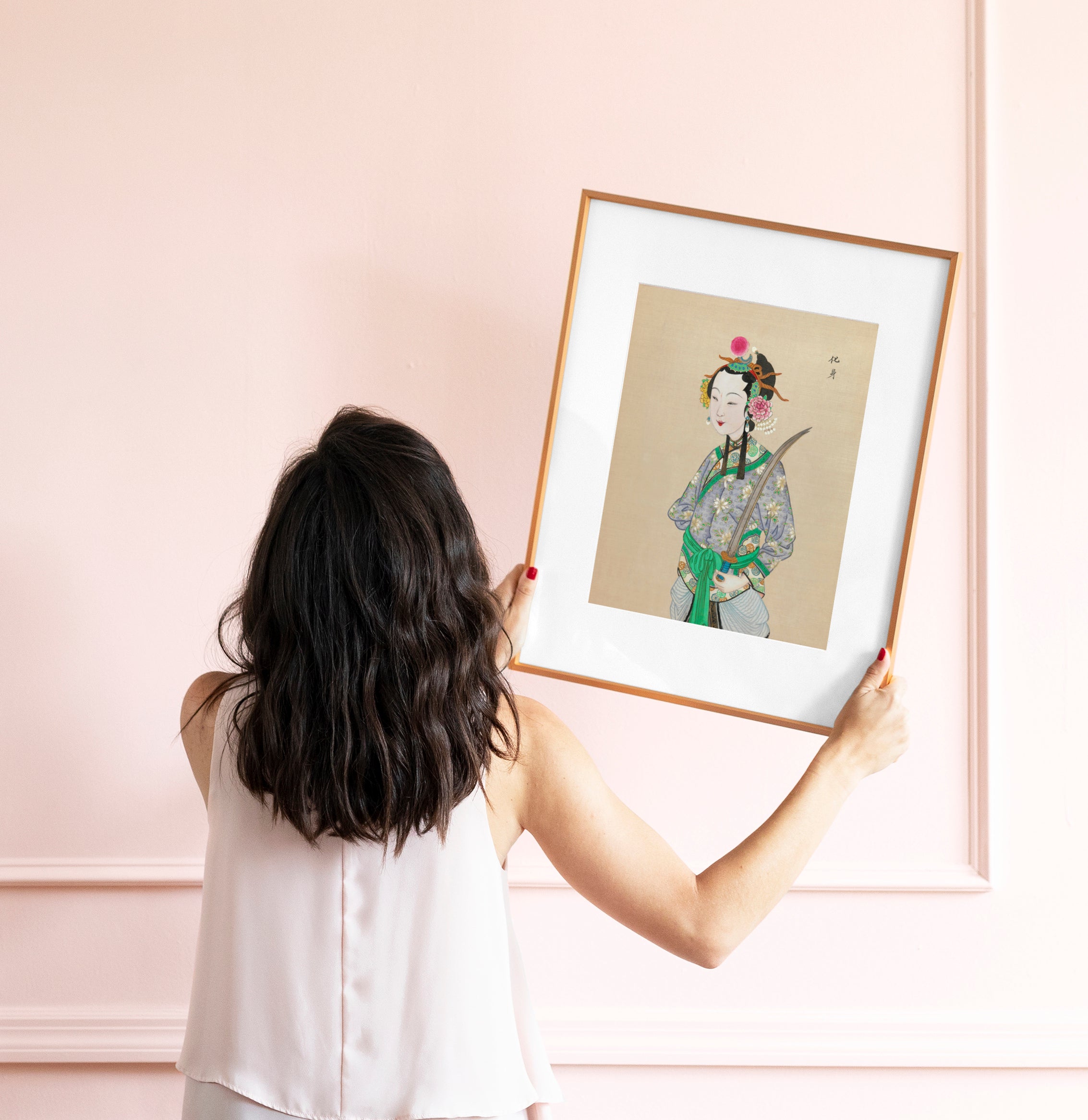 lady hanging chinoiserie print on pink wall