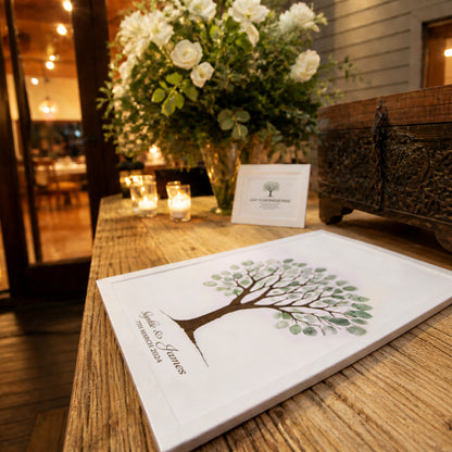 Rustic wedding guest book table with fingerprint tree print, candles and floral arrangement in warm lighting, styled as a unique guest book alternative for a wedding reception.