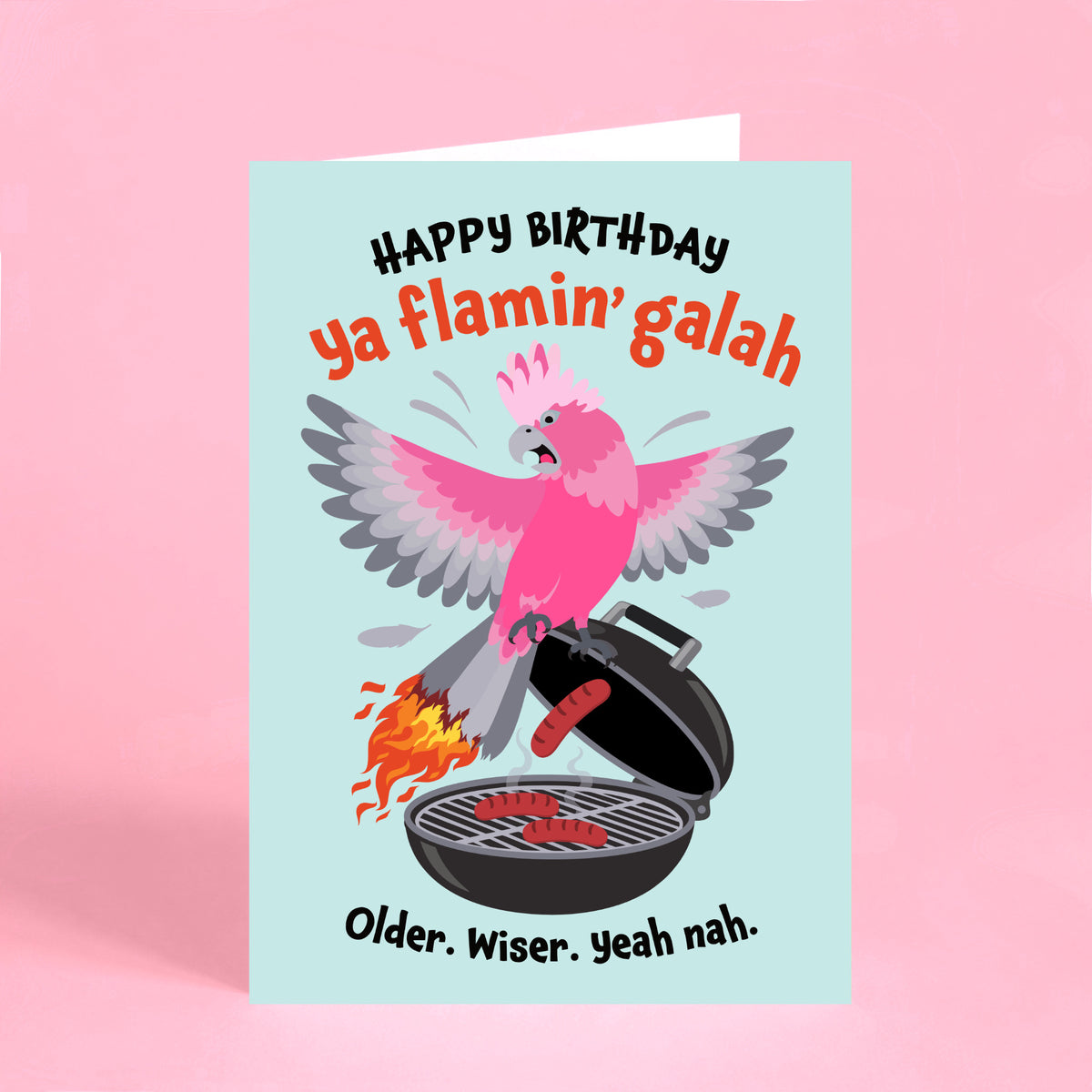 Funny Australian birthday card featuring a pink galah perched on a BBQ with flaming tail feathers and “Happy Birthday ya flamin’ galah” text.