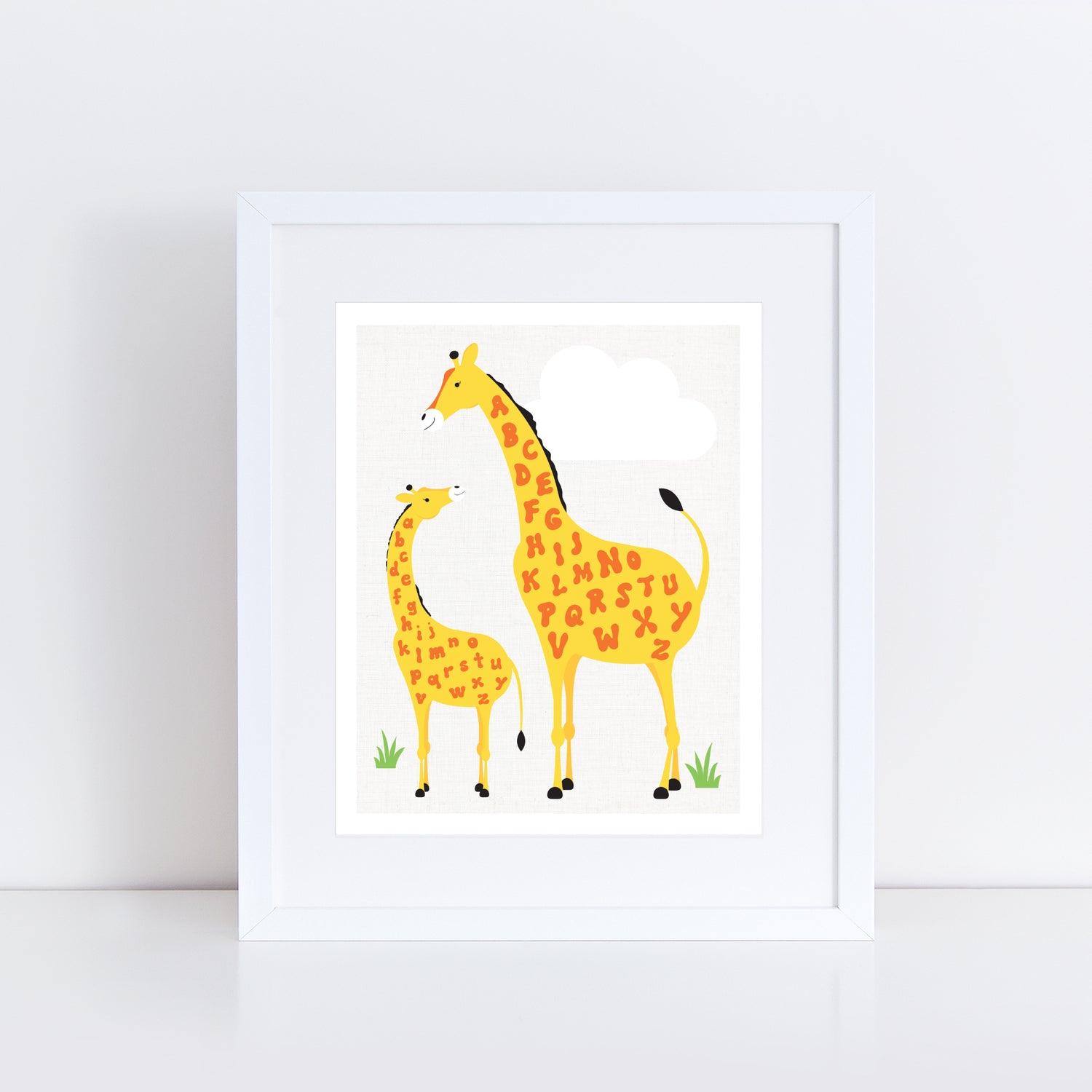 art print shows a tall parent giraffe and a smaller baby giraffe standing on grass under a white cloud. Both giraffes have bright orange alphabet letters scattered across their yellow bodies, creating a playful and educational design