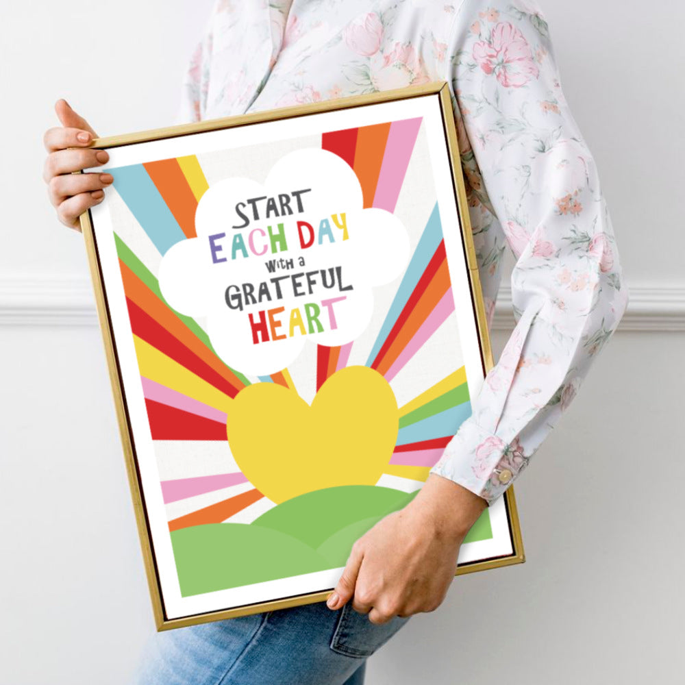 person carrying framed canvas print of a sunrise heart with rainbow beams of light and quote Start each day with a grateful heart
