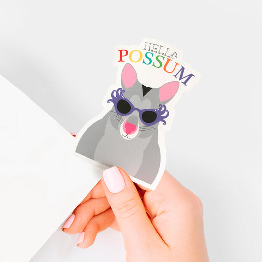 hand holding vinyl sticker with fun possum illustration and words hello possum