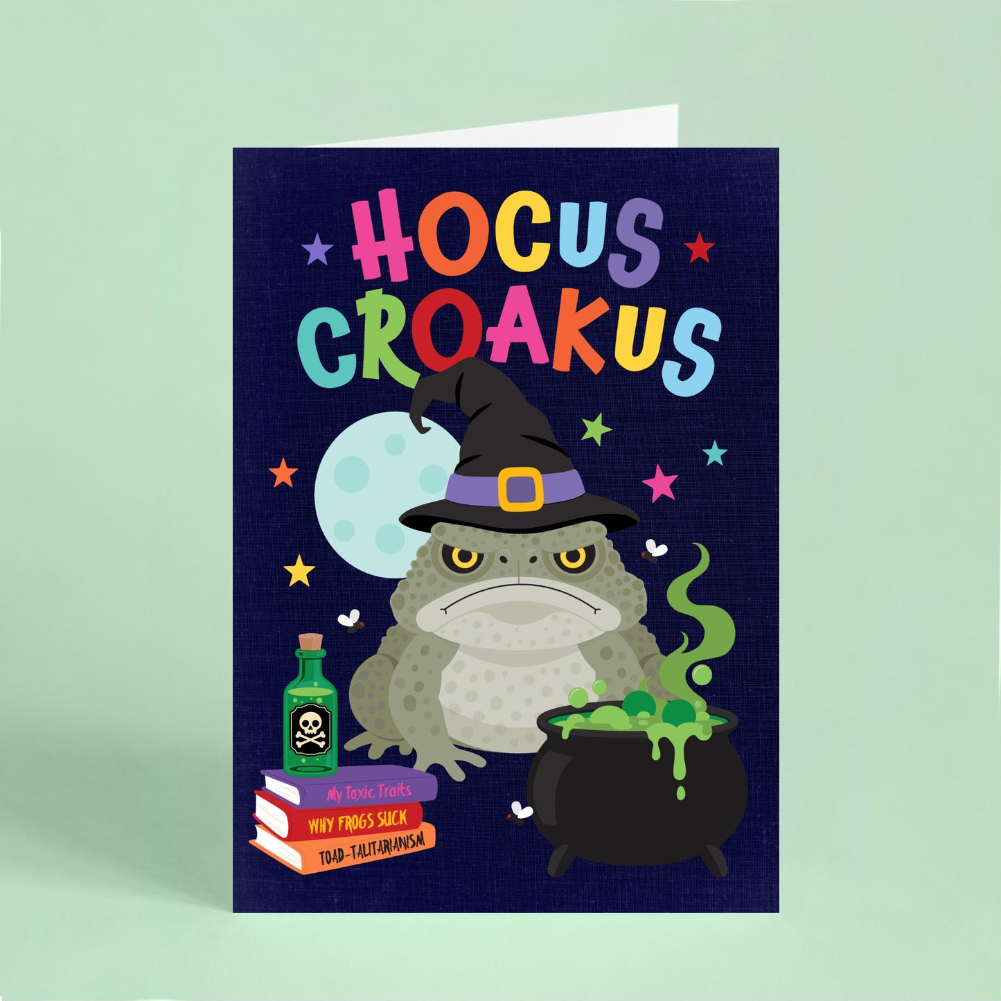 Funny Halloween card featuring a grumpy cane toad wearing a witch's hat beside a bubbling cauldron with the words "Hocus Croakus".