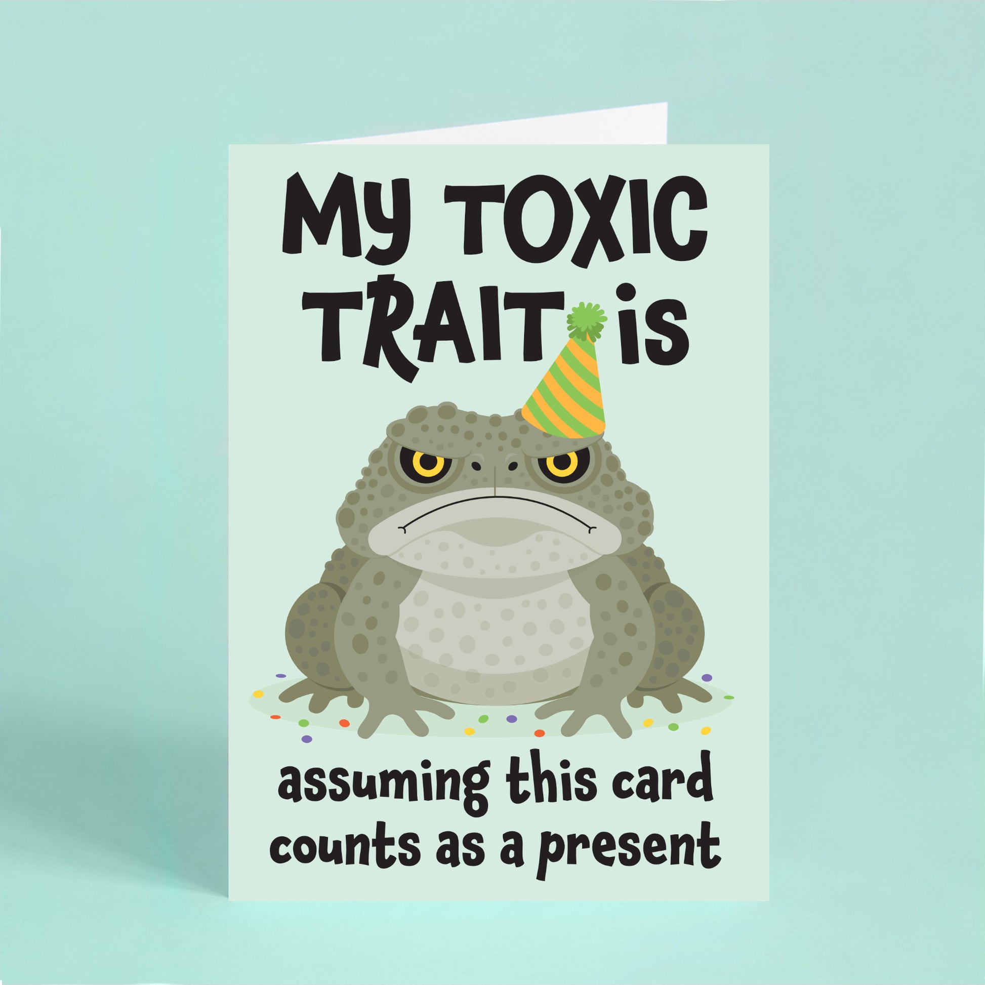 Funny cane toad birthday card featuring a grumpy toad in a party hat with the quote "My toxic trait is assuming this card counts as a present."