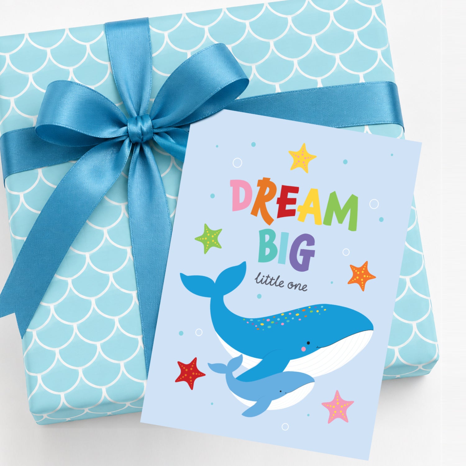 Colourful Dream Big new baby greeting card featuring a mother and baby blue whale with rainbow lettering, starfish and ocean bubbles, perfect for baby showers, newborn gifts and ocean-themed nursery celebrations sitting on top of a wrapped gift