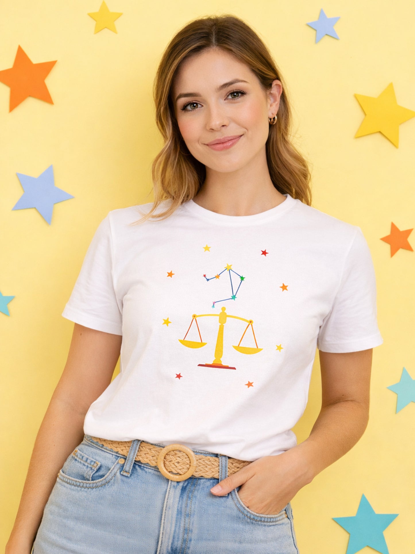 Woman wearing a white t-shirt with a colorful Libra zodiac sign design on a yellow background with star shapes.