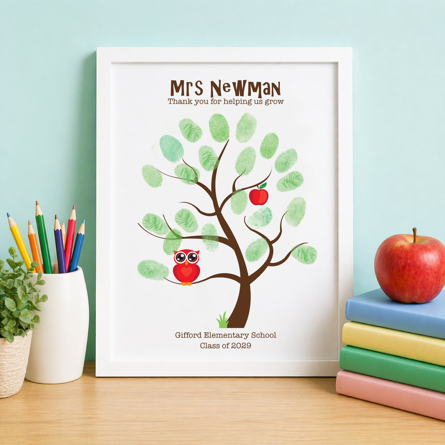 Fingerprint tree with owl and apples in a white frame, placed on a wooden surface with stationery items.