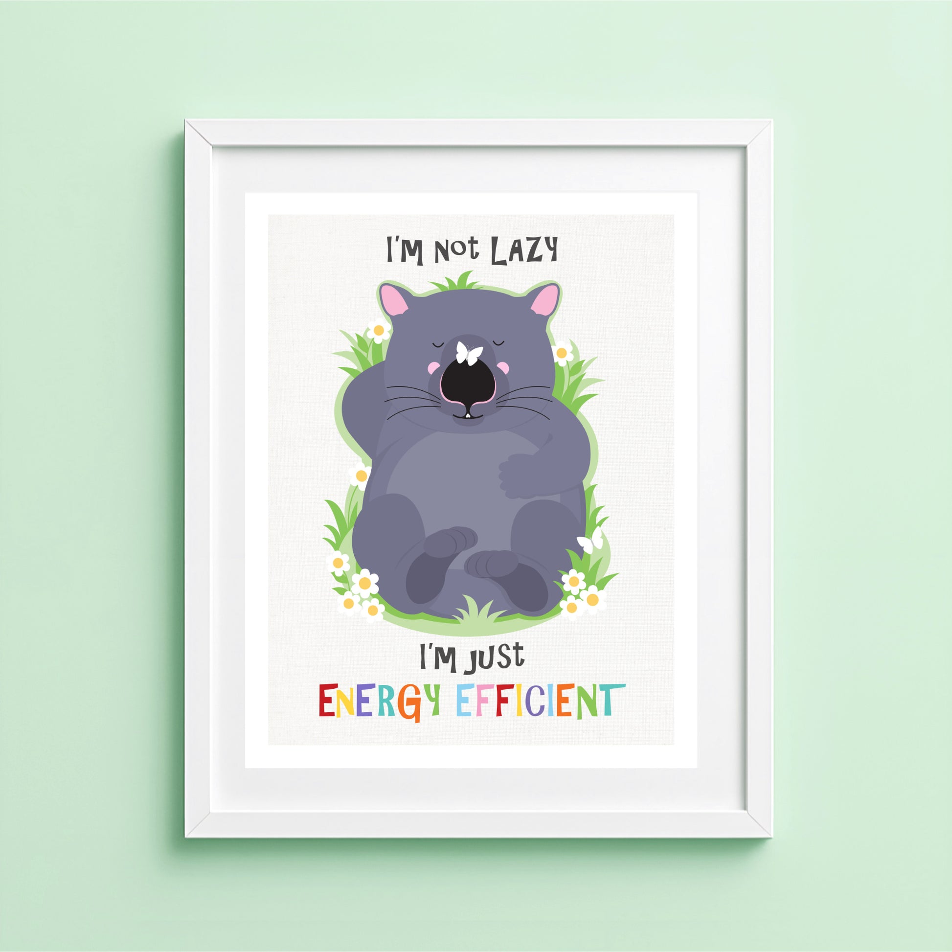 A cute illustrated wombat lies flat on his back, eyes closed, looking completely relaxed. The wombat is surrounded by a simple patch of green grass with a few small white daisies, set against a soft neutral background. Above and below the illustration, the text reads “I’m not lazy, I’m just energy efficient” in playful lettering. The overall style is flat, friendly, and minimal, with solid colours and a gentle, feel-good tone.