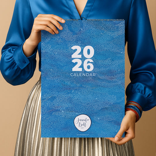 Person holding a blue abstract art calendar with '2026' printed on it 